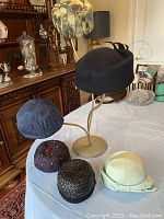 Six vintage hats displayed on a table with diverse styles and colors, showing the overall condition and design.