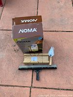 Photo of the Noma box with outdoor wall light, trowel, wooden blocks, and squeegee laid out on the ground