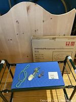 Front view of garden kneeler/bench with foam pad, wooden board behind it, boxed glass lazy susan, and two garden pins on top of foam padding.