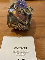 Front view of the metal cuff bracelet with large rough amethyst crystal and vine details on top and sides, showing used condition and polymetallic finish.