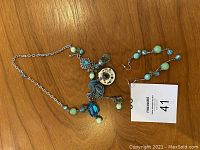 Photo showing the full turquoise glass necklace alongside the matching earrings on a wooden surface with a MaxSold card.
