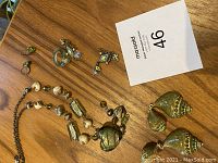 Photo showing Murano glass heart necklace, various rings, costume earrings and green shell clip earrings on wooden table.