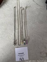 Five necklaces displayed on a grey surface including silver chain with pearl and blue stone pendant, heart-shaped pendant, turtle pendant with multicolored stones, small round colorful pendant, and purple enamel 'Mother' pendant.