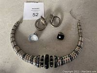 Vintage 1980's silver-tone necklace, two pairs of silver earrings, two rings, and a silver bracelet laid out on a flat surface