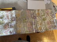 Silk scarf with floral pattern and tassels spread out on surface