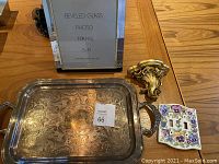 Silver serving tray, French gilded plaster shelf, beveled glass photo frame, and floral light switch plate arranged on wooden table