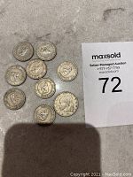 Ten Liberia coins, including nine 5 Cents coins dated 1961 and one 25 Cents coin dated 1960, laid out on a surface next to a MaxSold card with lot number 72.