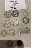 All 12 Portuguese coins arranged on a stone surface showing both $5 and smaller denomination coins with ship designs.