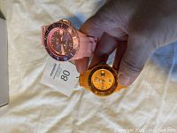 Close-up of both Ice Watches held in hand showing front dial details and color (pink large and orange medium).