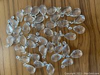 Top view of 40 clear, teardrop-shaped chandelier crystals arranged on a wooden surface.