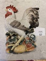 Full view of ceramic rooster wall hanging showing overall shape, colors, and base details with fruits and leaves.