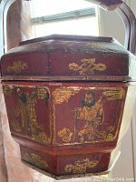 Front and side view showing the painted decorative figures in gold on red background, octagonal shape with a fitted lid
