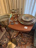 Wide shot showing all items on wooden table including plant stand, plates, vases, candlesticks, and hanging brass decor.