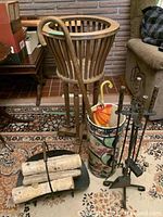 Photo showing wooden plant stand, ceramic umbrella stand with umbrella, metal log holder with firewood, and fireplace tools on a rug.