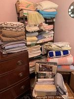 Overview of linens, towels, sheets and vintage curtains stacked on metal shelves and wooden chest.