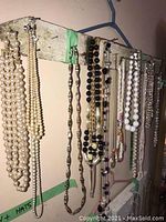 Necklaces hung on worn wooden board showing various pearls, chains, and beaded necklaces.
