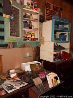 Wide view showing antique dressers, medicine cabinet with vintage supplies, blue tins on shelving, and red vise