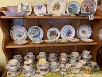 Full shelf display showing multiple plates on top two shelves and tea cups with saucers on bottom shelf