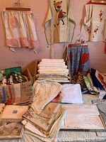 Overall view of table linens spread on table, including aprons hanging on wall, stacked linens, and box of towels