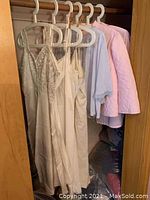 Five vintage lingerie and bed jacket pieces hanging on wood and plastic hangers inside a closet.