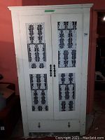 Front view of white painted wooden armoire with decorative vented panels and ornate metal handles.