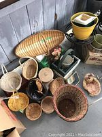 Photo showing multiple wicker baskets of various shapes and sizes on the ground near a green plastic outdoor chair and yellow plant stand.