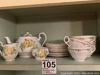 Shelf with Grindley Creampetal bone china teapot, sugar bowl, creamer, cup, saucer, and plates with floral yellow roses and gold trim.