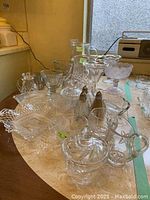 Photo showing an assortment of clear cut glass serviceware including pitchers, bowls, and shakers arranged on a table with light reflections