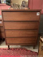 Front view of mid-century modern four-drawer dresser with wood veneer and tapered legs, showing overall condition.