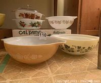 Overall image of the vintage baking dishes and mixing bowls set on floor, showing variety of Pyrex bowls and covered casserole in stacked arrangement
