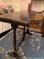 Full side view of the vintage wood hall/library/sofa table showing table top, turned legs, and stretcher base on floral carpet.