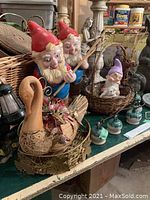Photo of two garden gnome statues with fishing poles, swan-shaped basket, woven baskets, and small ceramic bird figurines on a table.