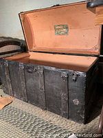 Open view of black dome-shaped steamer trunk showing interior painted peach with decorative label on lid