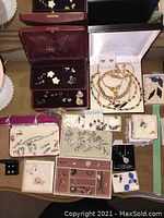 Overview of multiple open jewelry boxes containing bracelets, necklaces, earrings; partial view of milk glass lamp shade.