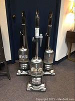 Three gray Shark Navigator LiftAway upright vacuum cleaners with clear dust canisters, shown from front.