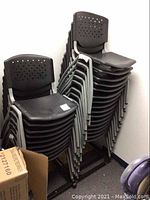 Stacked black plastic and metal chairs showing triangular cut-out design on backrest and metal legs, arranged on two rolling metal stands.