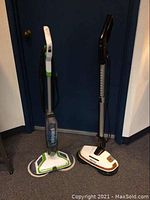 Front view of two electric mops side by side against a blue door, Bissell SpinWave on left, Elicto on right