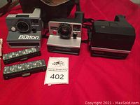 Photo showing three vintage Polaroid instant cameras: The Button, Pronto!B, and Sun 600, along with two Flash Bars.