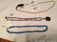 Three necklaces laid out on a white cloth, showing different bead colors and styles, with auction lot tag.
