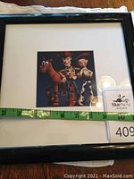 Framed Toy Story print showing Woody, Jessie, and Bullseye in black frame, measuring approximately 12 inches square with tape measure visible