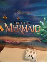 Close-up photo of sealed original packaging for Disney's The Little Mermaid promo lithographs showing underwater scene with fish and coral and movie title.