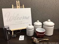 Photo showing all items in the lot including storage canisters, bowls, serving spoons, welcome sign on easel, and the soap dispenser