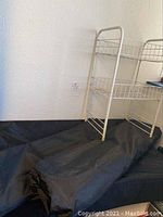 Folded flat black under bed storage bags shown stacked on a black fabric background with a white wall behind.