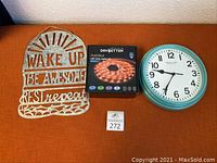 Lot items displayed on orange surface: decorative metal sign, unopened LED strip light box, turquoise framed clock