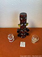 Front view of ceramic totem pole liquor decanter with four attached mini cups and three glass votive candle holders.
