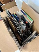 Photo showing a cardboard box filled with various folded and flat cardboard magazine holders and box templates in assorted colors and designs.