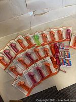 Lot of 24 personal mini fans mostly orange and pink with one green, all in original packaging with batteries on white surface.