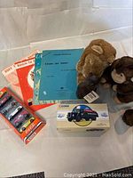 Overview photo showing the monkey and lion hand puppets, Ironwood cat figurine, Matchbox toy cars pack, Corgi petrol tanker boxed toy, and vintage sheet music.