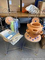 Two wrought iron chairs with decorative terracotta and blue tile mosaic seats and backs. One chair holds the terracotta strawberry pot and other items.