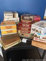 Full view of assorted cigar boxes stacked on a black cart against a blue background